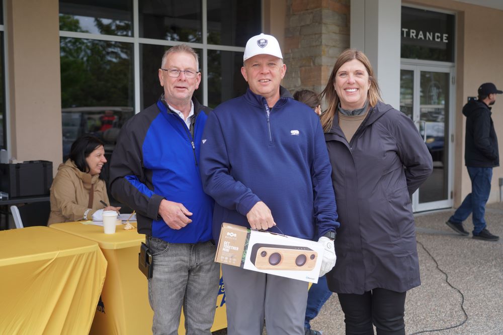 President Kelly Tosato and Secretary-Treasurer Jim McLean stand together with a golfer at the Locals tournament 2025.