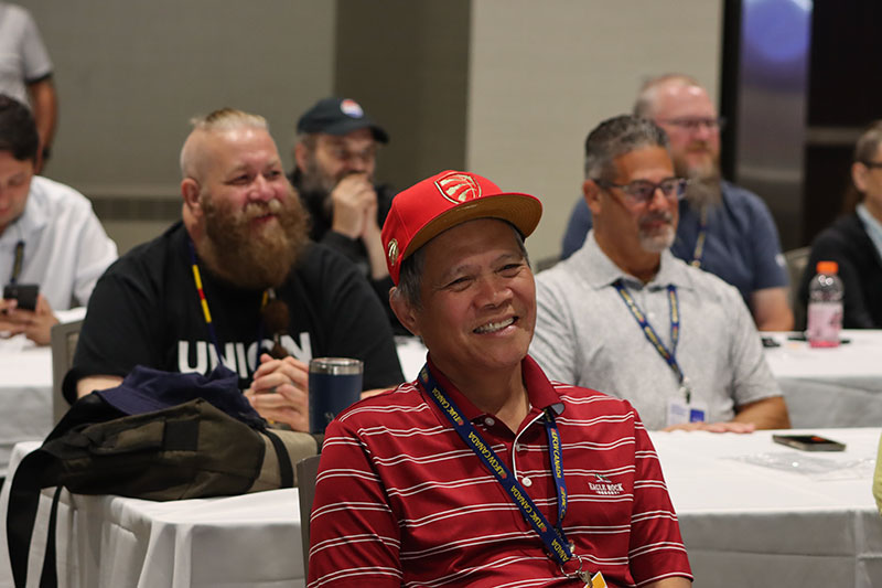 Focus on a person smiling/laughing, with others blurred in the background similarly smiling, as they react to a speaker at the convention.