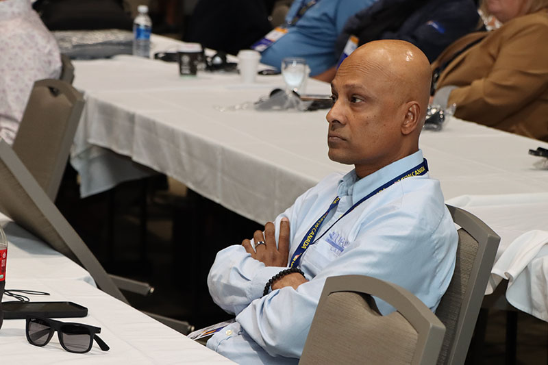 A person with their arms folded across their chest sits at a table in the audience.