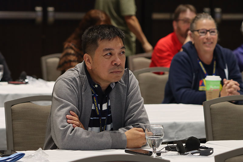 A person who is seated looks attentively toward the front of the room during a convention presentation.