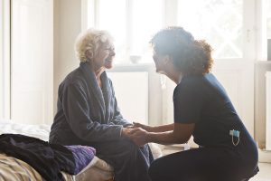 A healthcare provider and an elderly person are seated and holding hands.