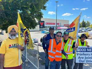 Five people in UFCW gear with UFCW flags rally employees outside an Ottawa Canadian Tire store.