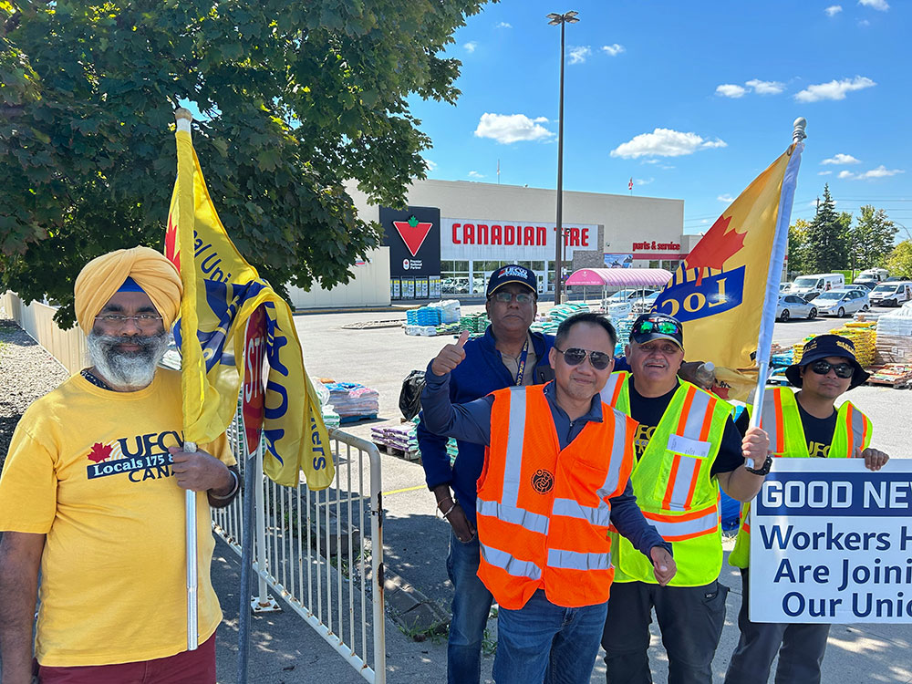 Five people in UFCW gear with UFCW flags rally employees outside an Ottawa Canadian Tire store.