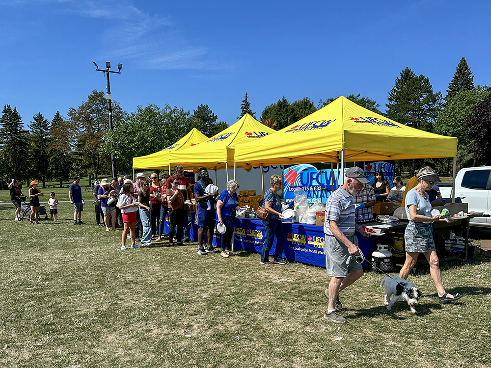 Labour Day 2025 in Cornwall where a number of people are lined up at UFCW tents for a barbecue lunch.