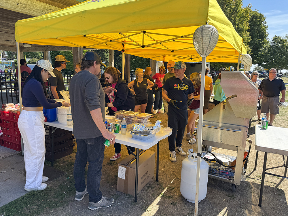 A group of volunteers barbecue lunch and help guests gather their food under yellow UFCW tents in Cobourg.