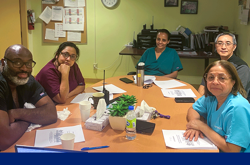 five Aramark Sherbourne members in scrubs seated around a table with copies of a memorandum of settlement