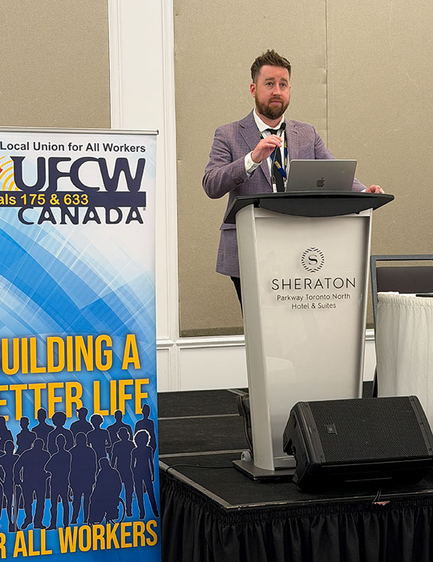 Regional Director Jason Hanley adjusts a microphone while standing at a podium next to a union banner