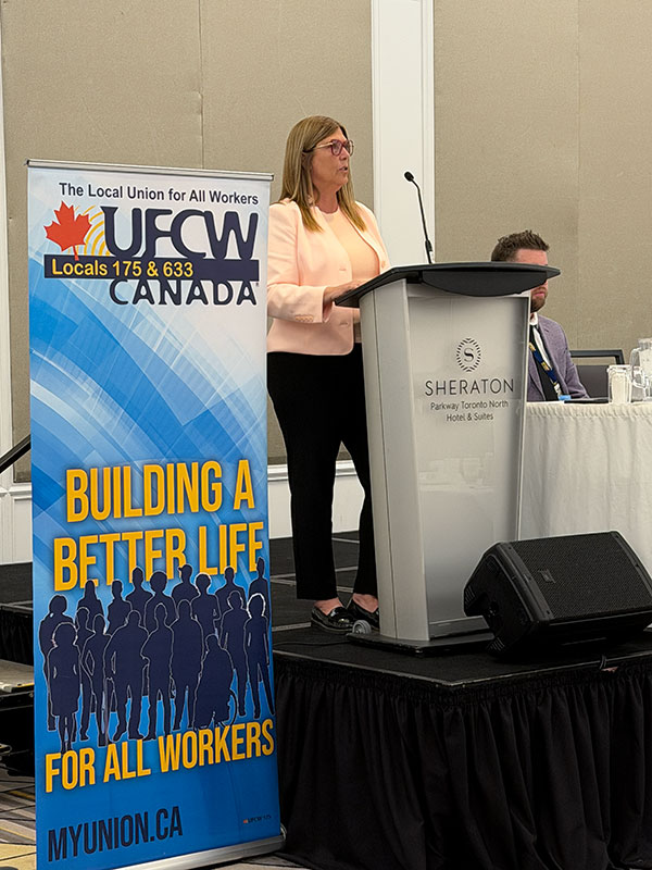 President Kelly Tosato speaks at a podium with a microphone next to a union banner