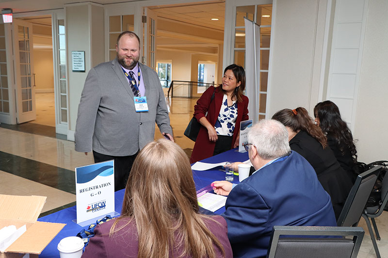 Two smiling people face a group of 4 seated union staff at conference registration