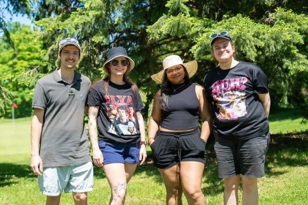 Four golfers smiling in front of some golf course trees.