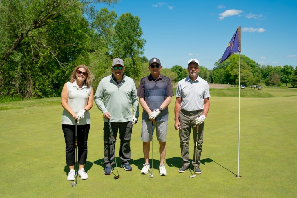 Four golfers smiling beside the flag stick.