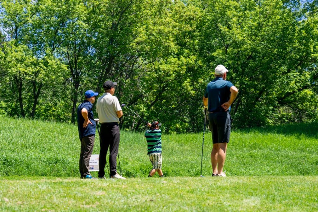 Three golfers watch their teammate hit the ball.