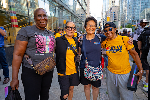4 people standing with their arms around each others' shoulders, smiling