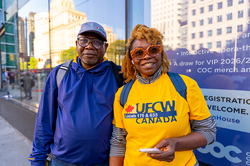 2 people smile for the camera; 1 is in a yellow ufcw shirt, the other wearing a blue jacket and ufcw hat