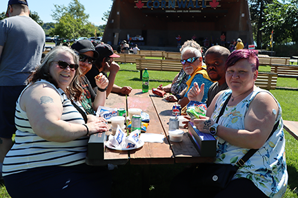 7 people seated at a picnic table with the Cornwall bandstand in the background