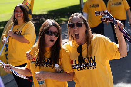two people yell in solidarity as they march in the hamilton parade & a person behind them smiles