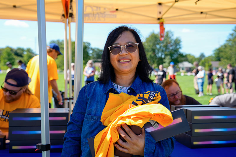 a person smiles warmly as they hold their union tshirt and the logo'd speaker they received as a gift at registration