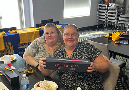 two people seated with UFCW table cloths and shirts in the background. person in the foreground is holding a portable speaker