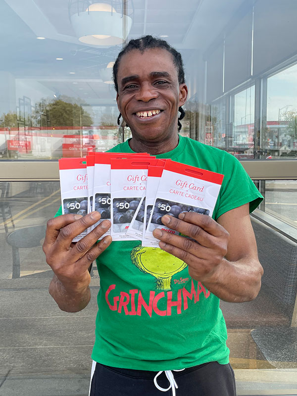 Efandieu Jesura holds up several gift cards while standing outside in front of a glass window of a business